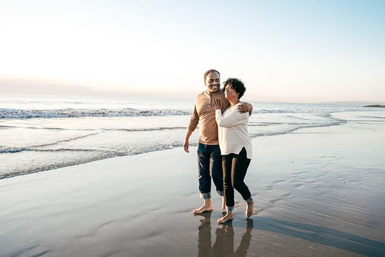 An older couple walking on the beach, the man has his arm around her shoulder